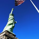 Statue of Liberty in front USA flag under blue sky